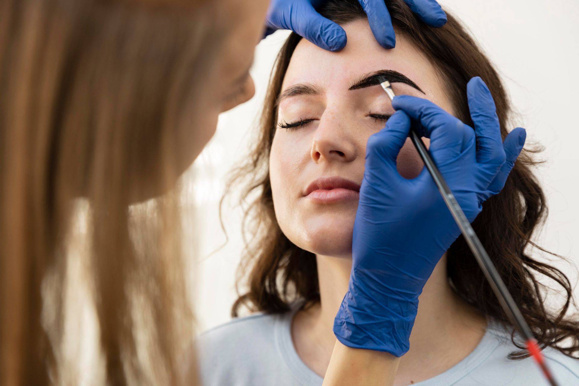 A woman is getting her eyebrows painted by a makeup artist in training.