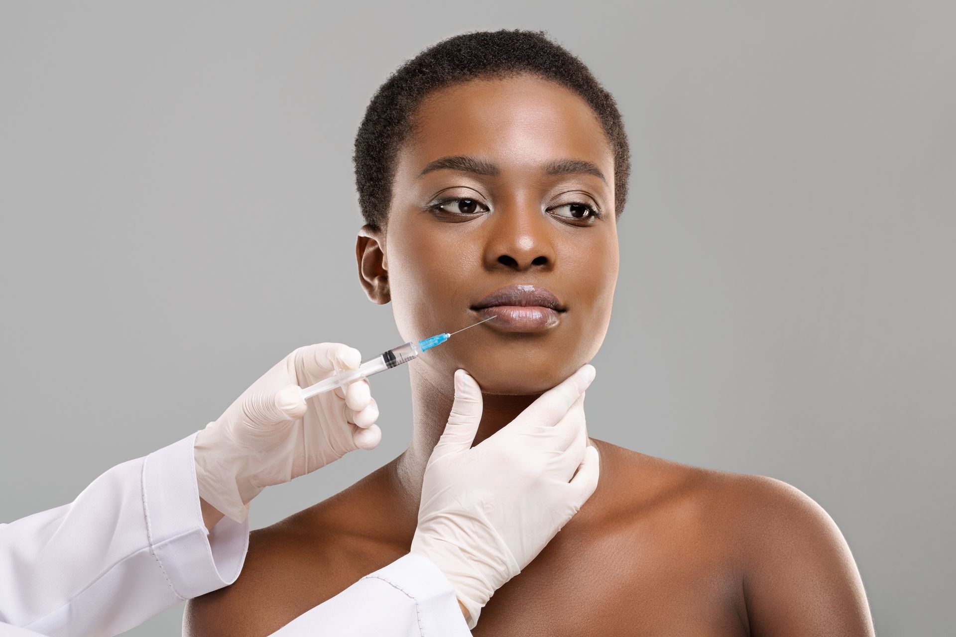 An attractive young African woman is getting rejuvenating facial injections from a beautician who i.