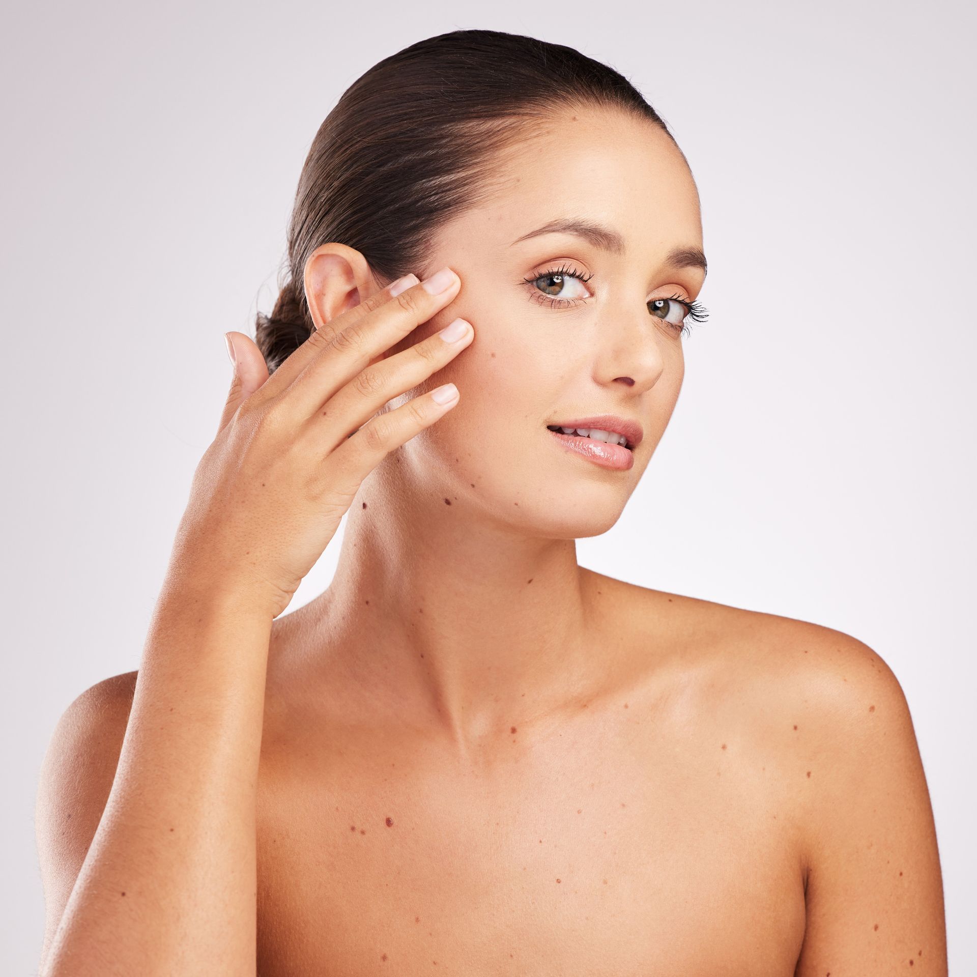 Woman touching her face, smiling. Neutral background. Bare shoulders.