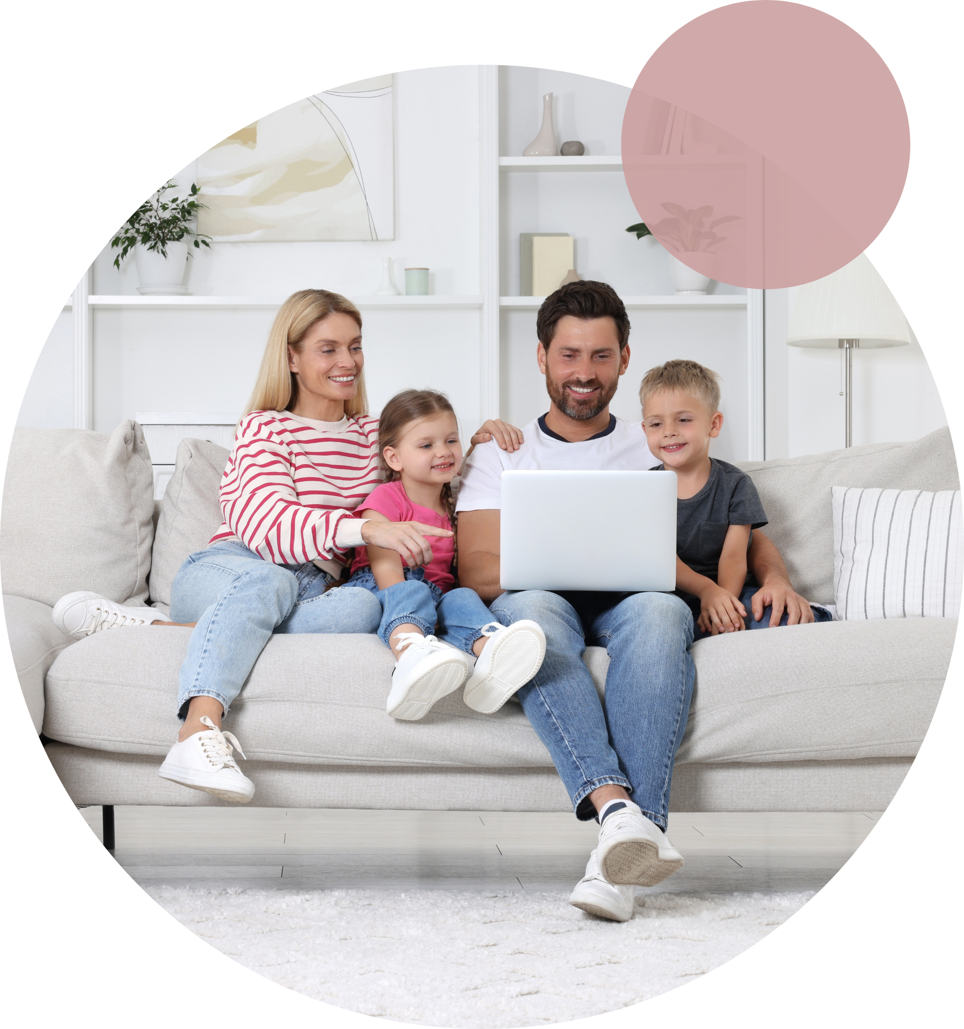 A family of four sitting on a white couch while looking at a laptop.