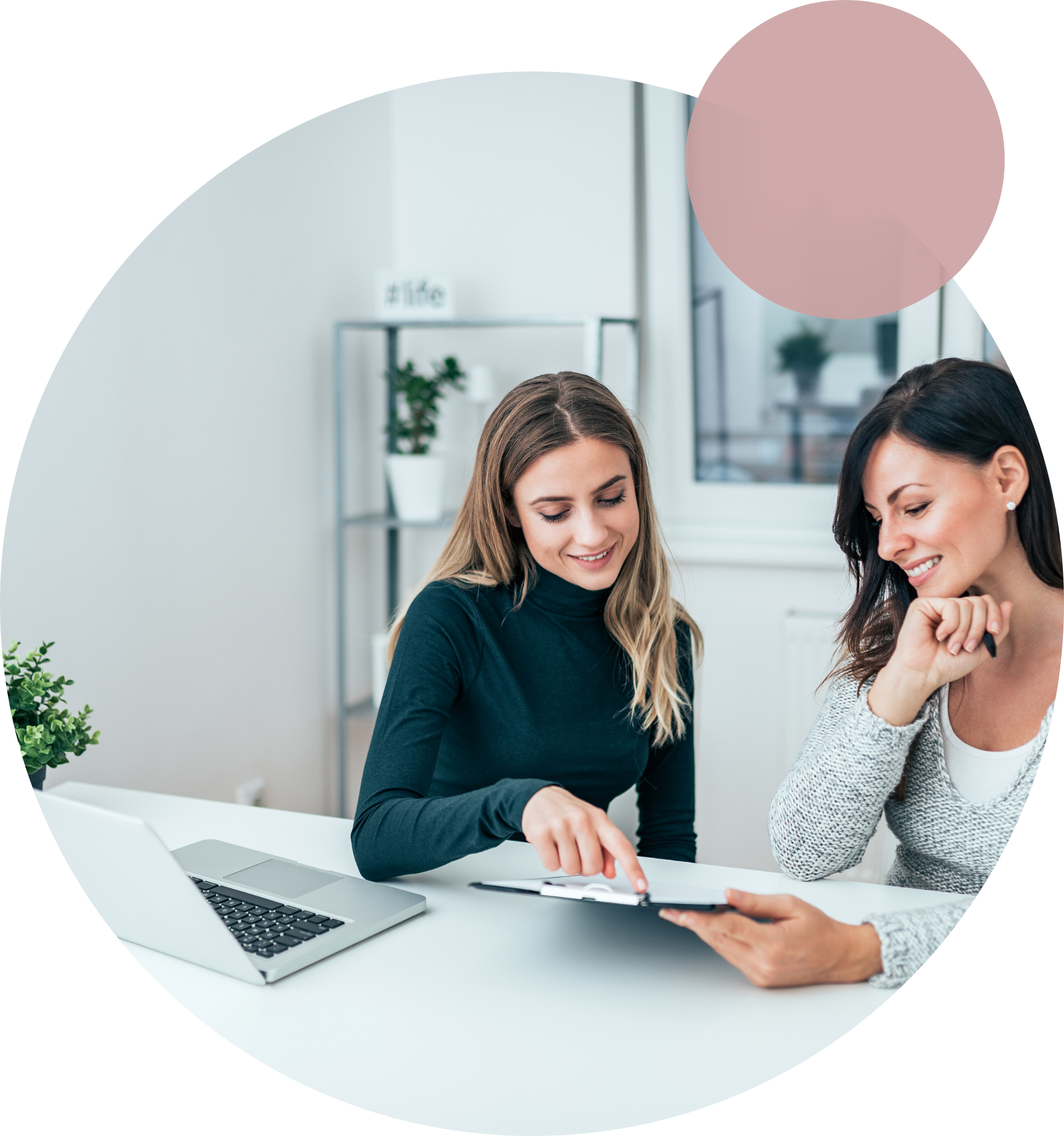 Two girls smiling and seated in front of a laptop while looking at a document.