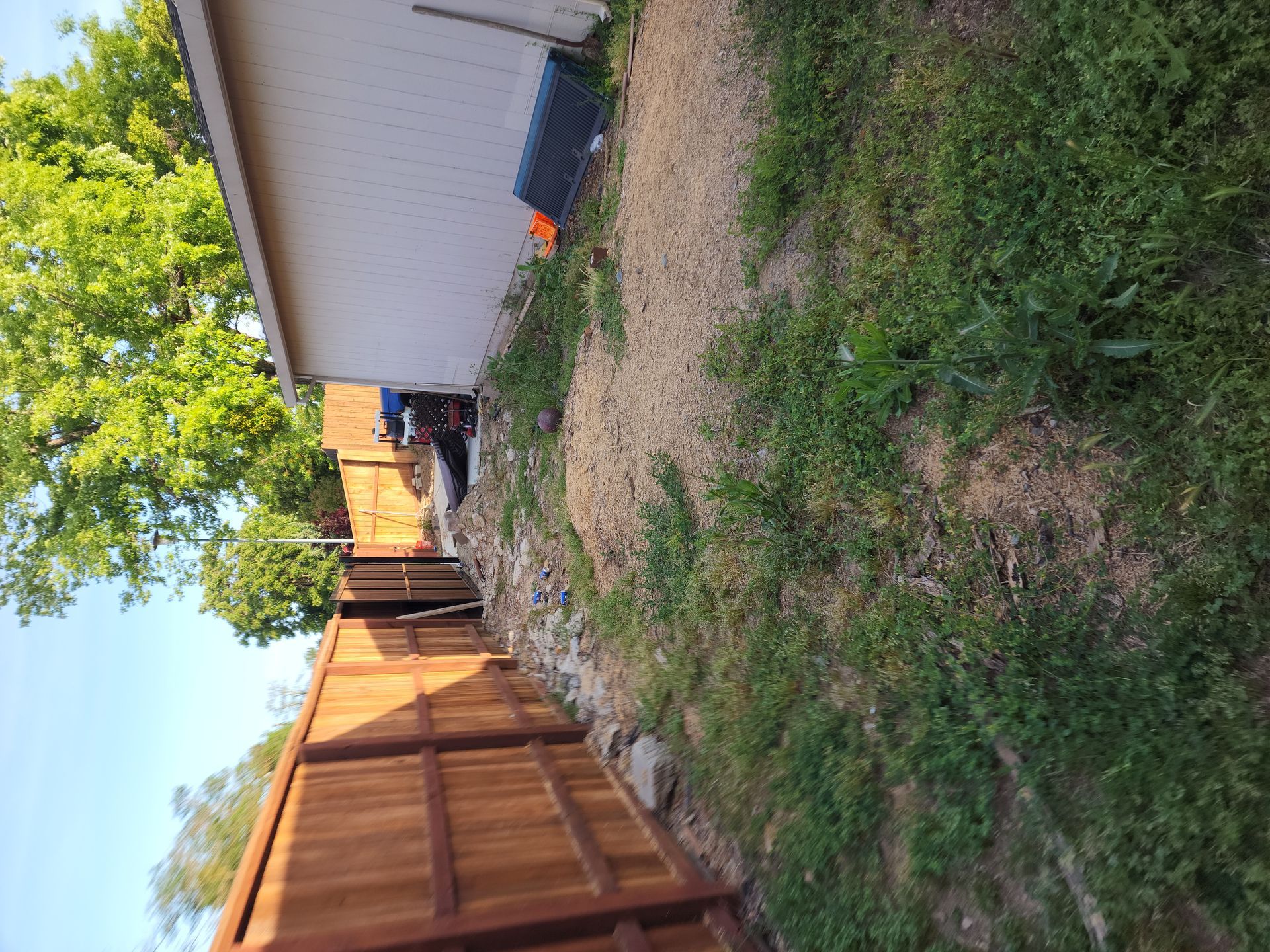 A wooden fence is surrounded by grass and dirt in a backyard.