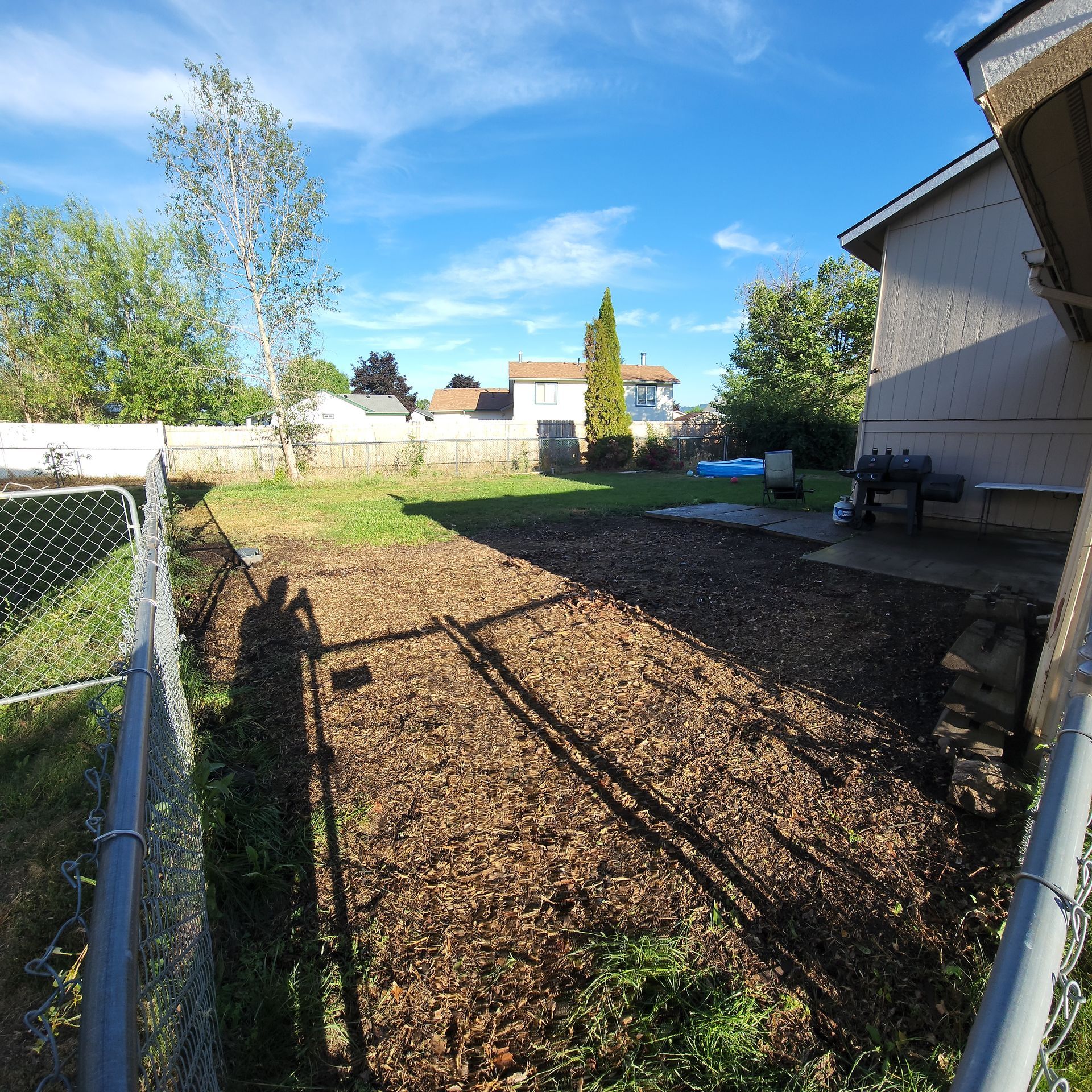 A backyard with a chain link fence and lots of mulch