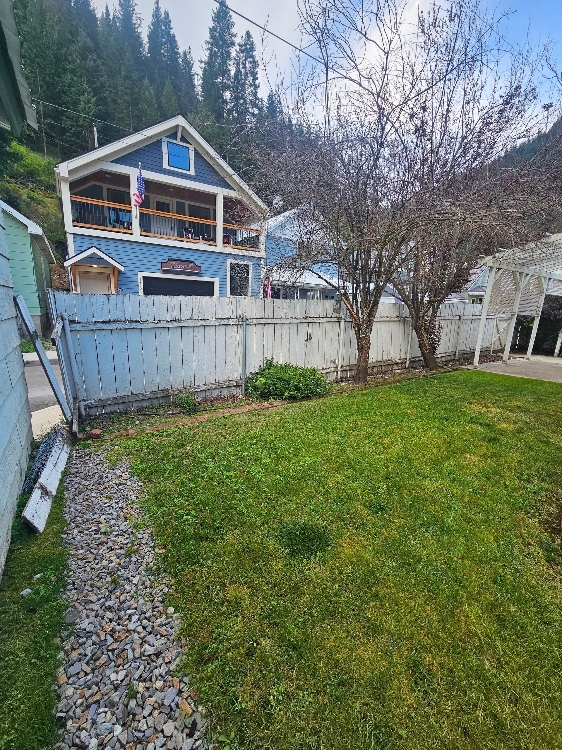 A blue house with a white fence and a large lawn in front of it.