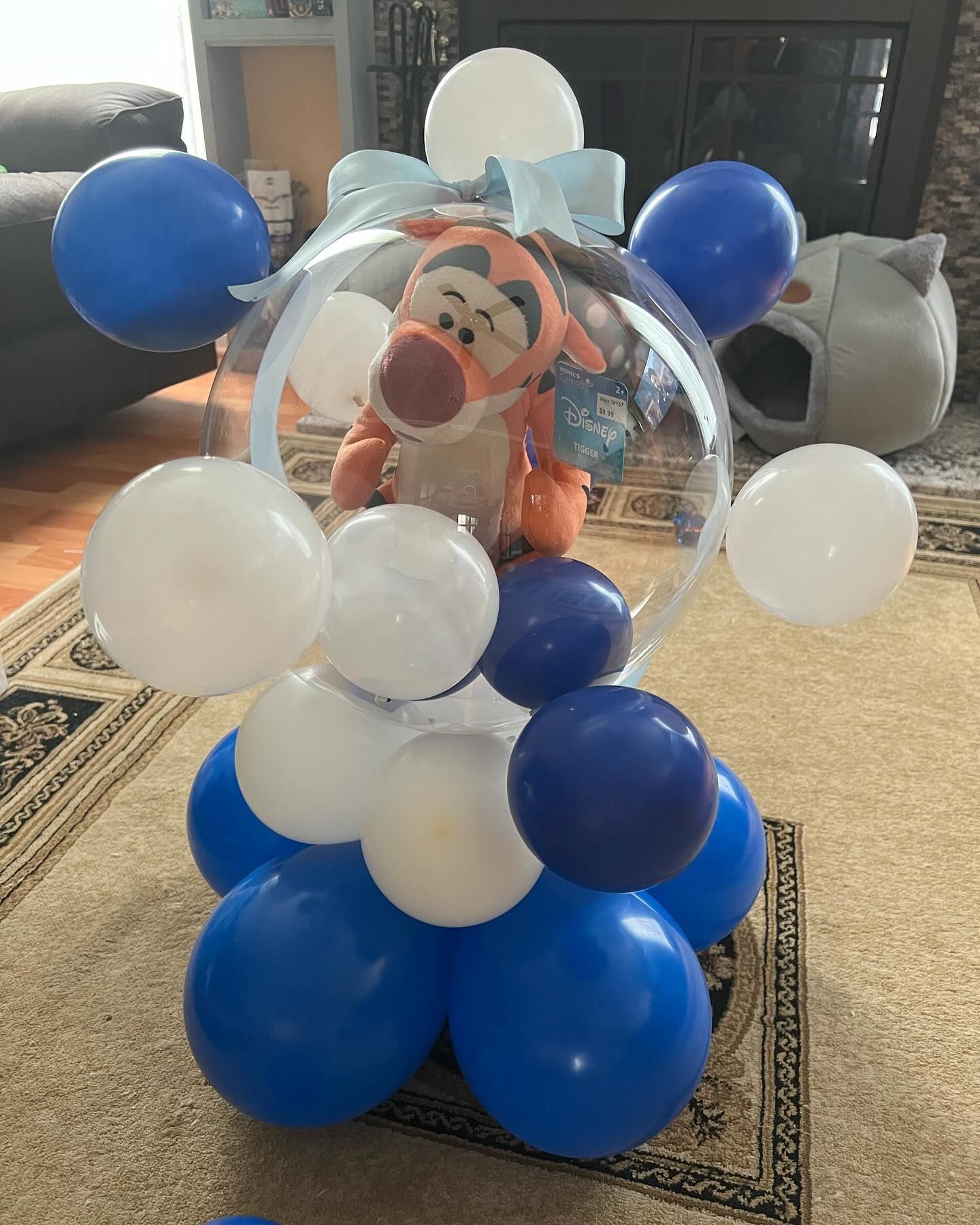 A stuffed animal is sitting inside of a clear balloon surrounded by blue and white balloons.