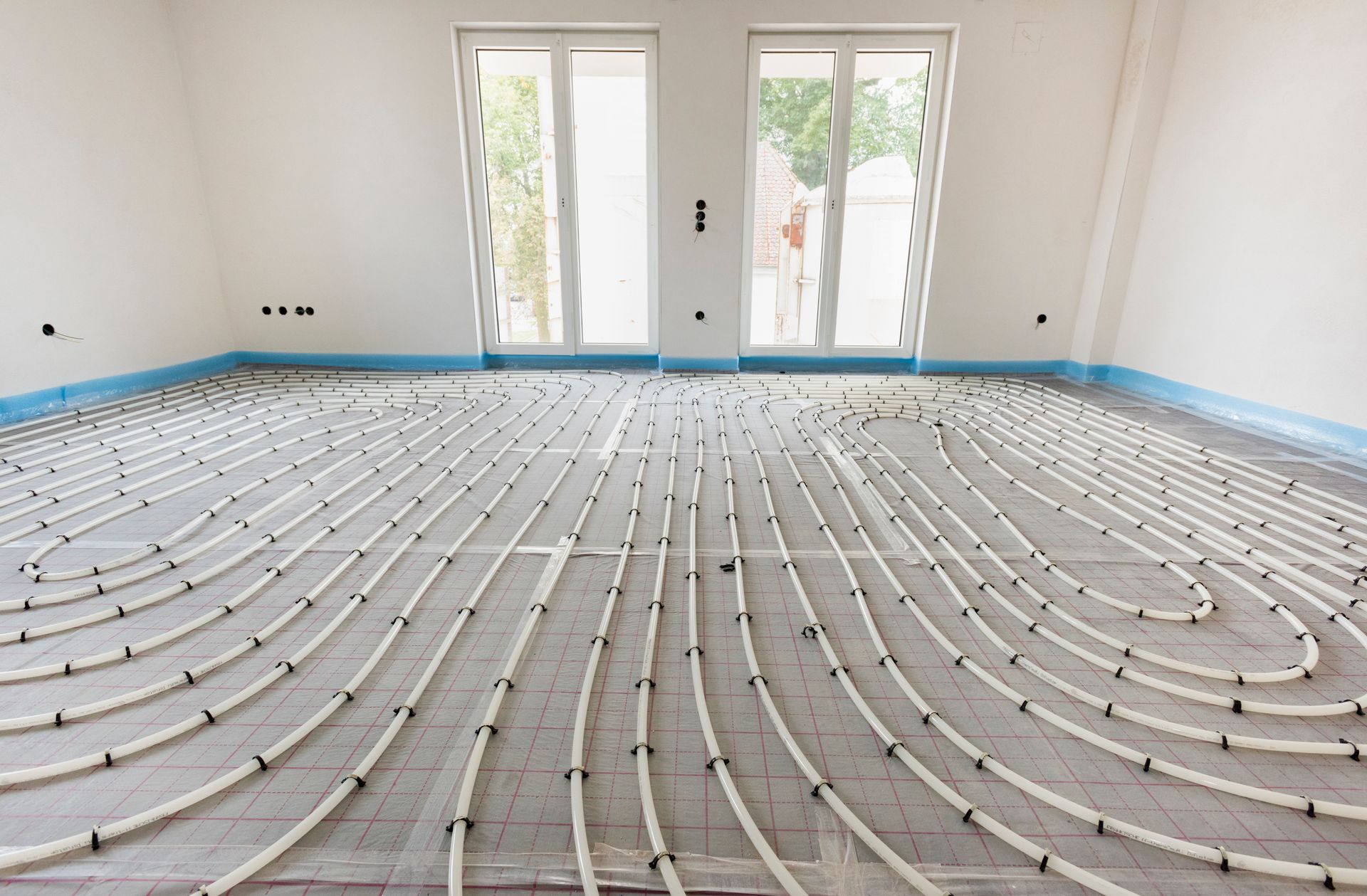White room with floor heating pipes laid out; windows in the background.