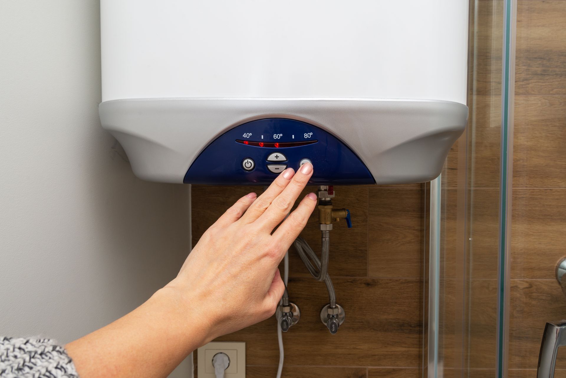 Person's hand adjusting the controls of a white and blue water heater in a bathroom.
