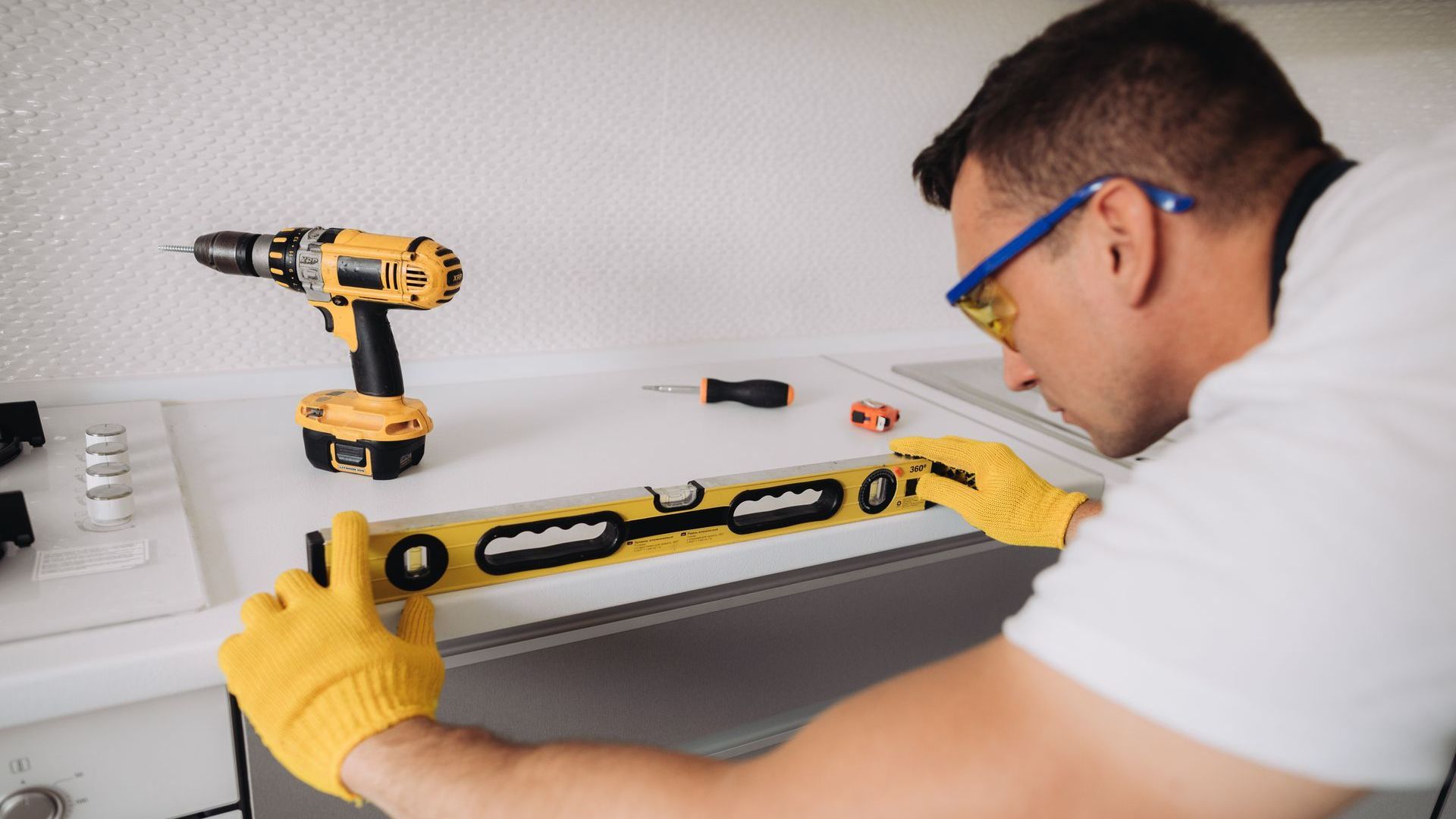 A man is working on a kitchen counter with a drill and a level.