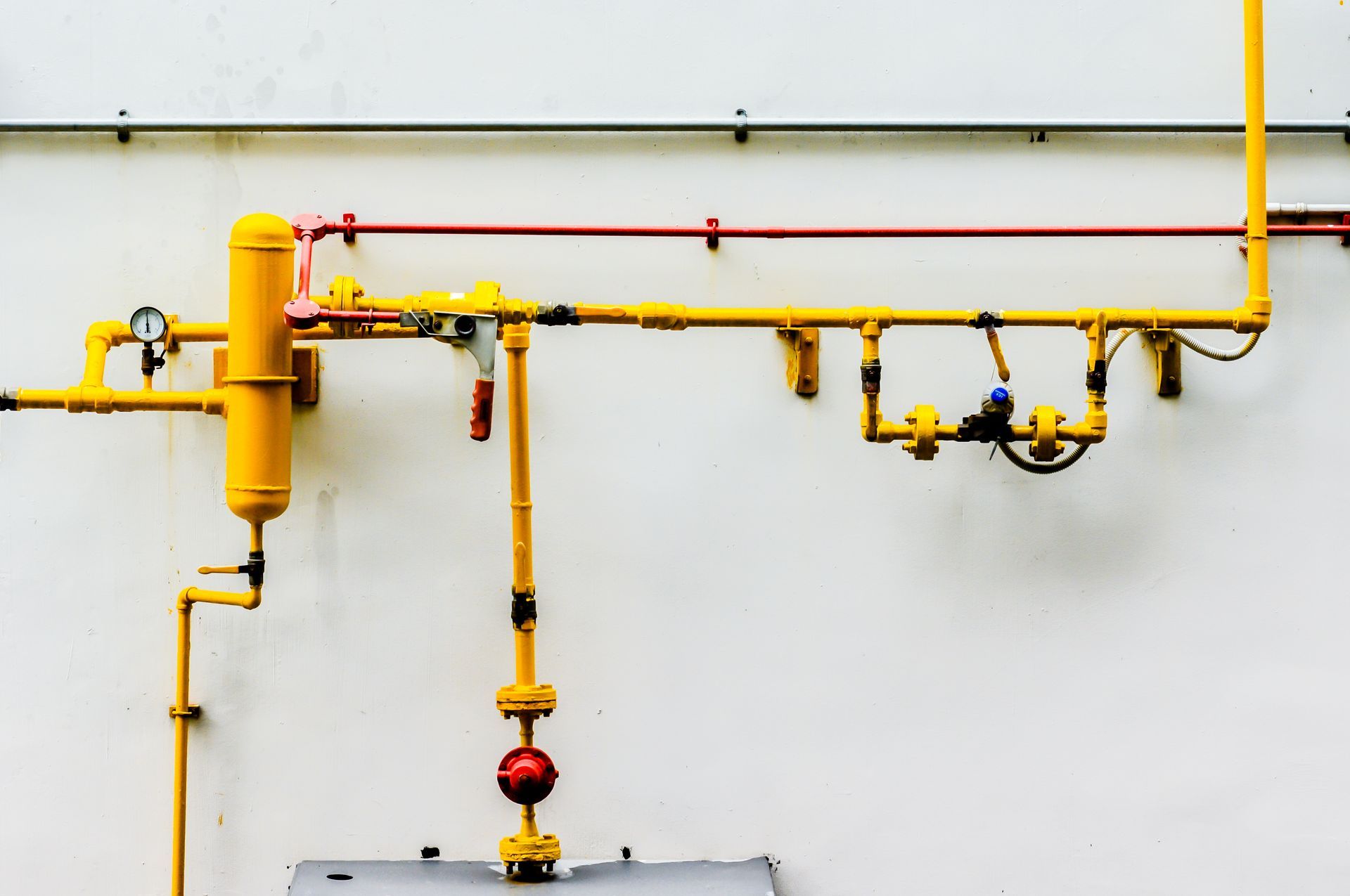 Yellow and red pipes on a white wall with gauges and valves, likely for gas or another fluid.