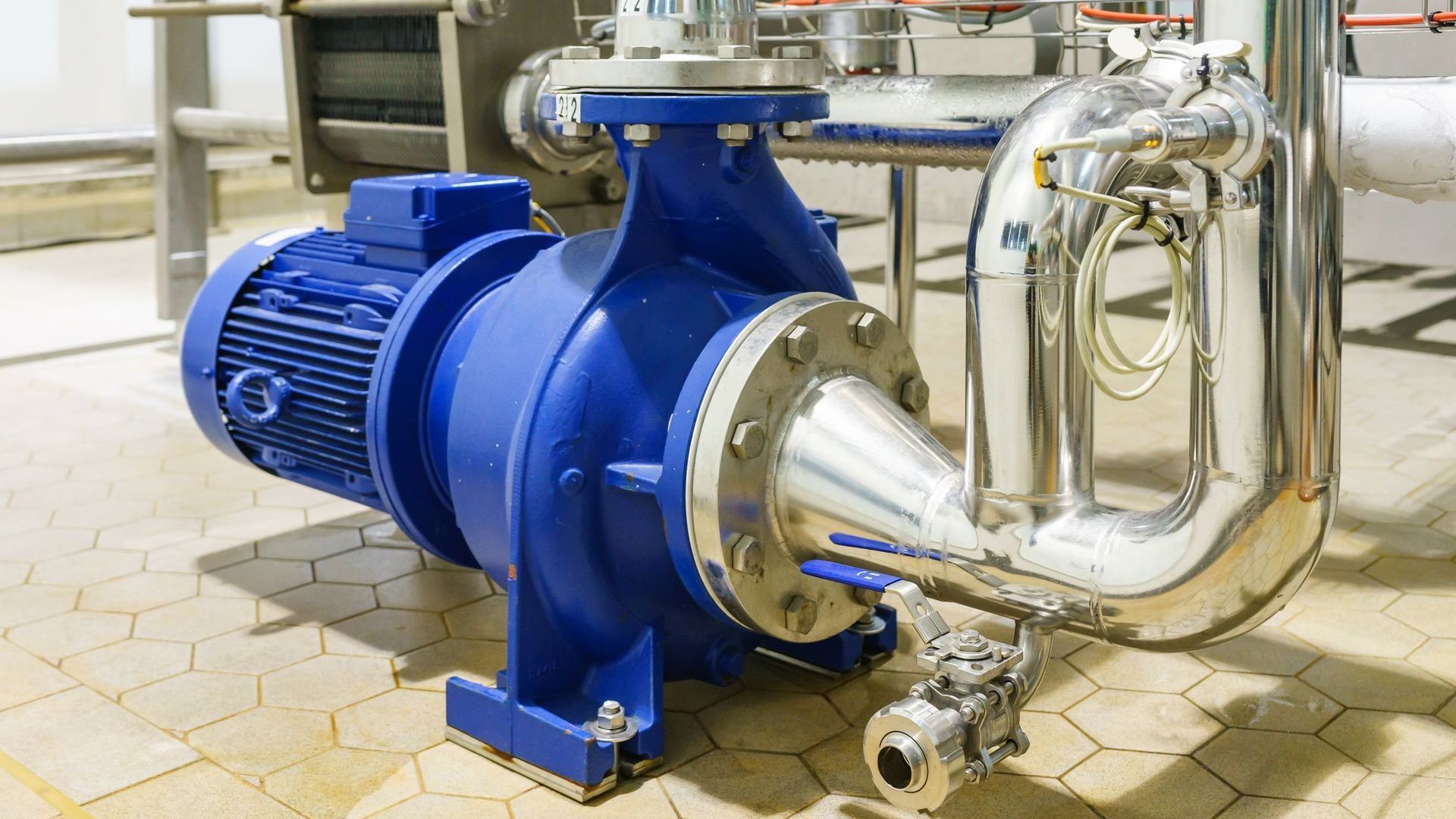 A blue water pump is sitting on a tiled floor in a factory.