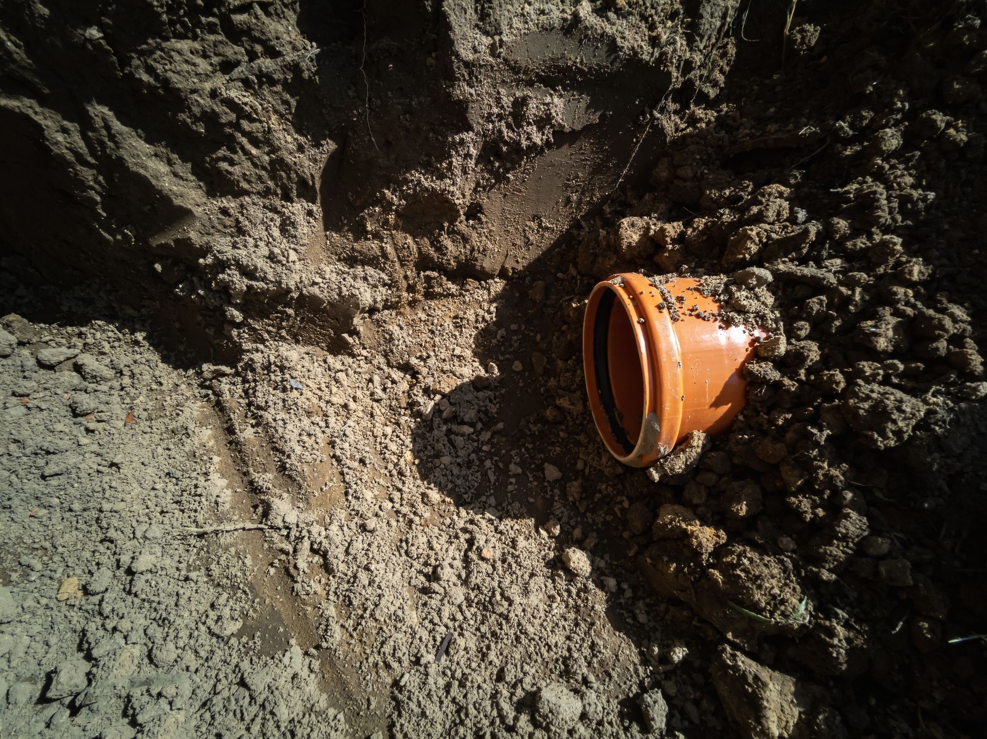 An orange pipe is laying in the dirt on the ground