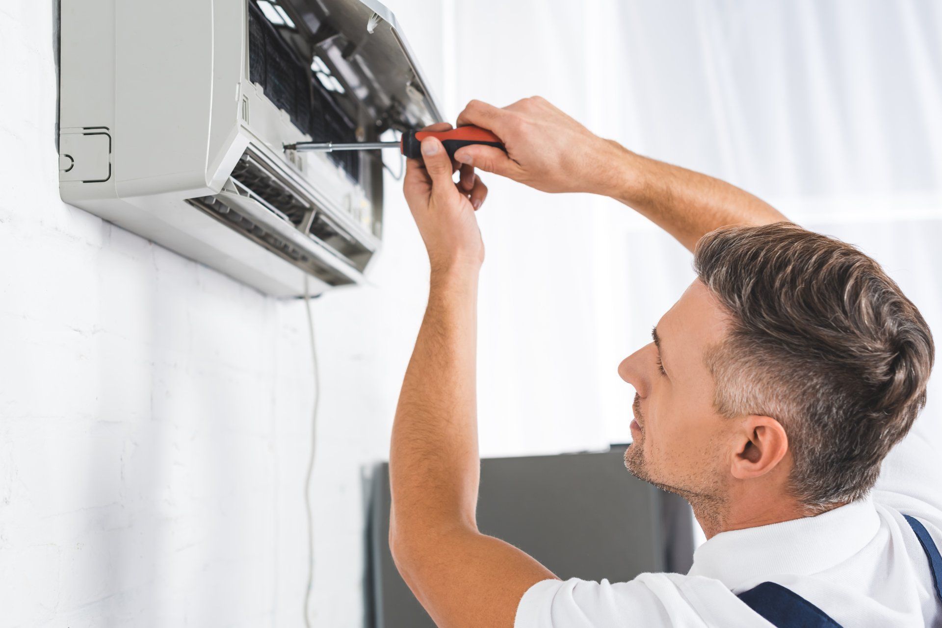 A man is fixing an air conditioner with a screwdriver.