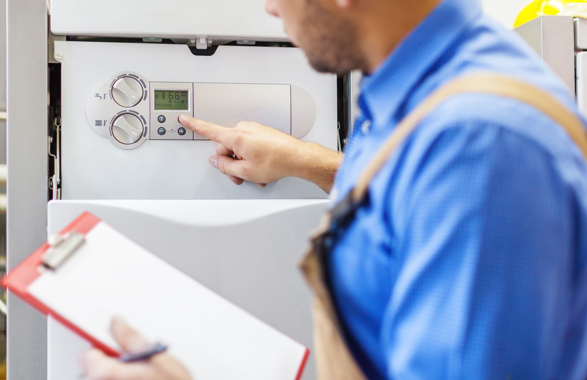 A man is working on a boiler while holding a clipboard.