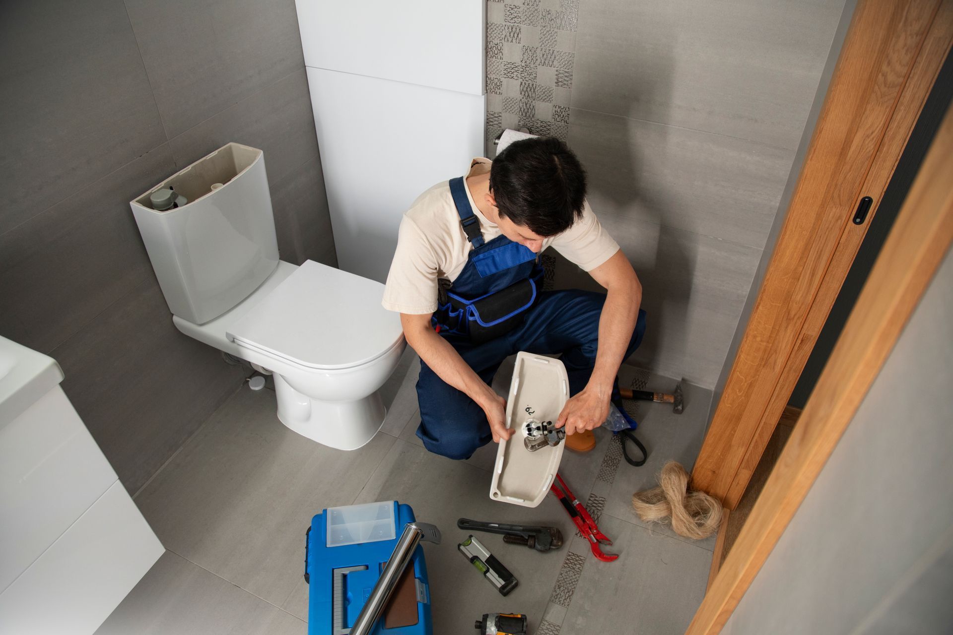 A plumber is fixing a toilet in a bathroom.