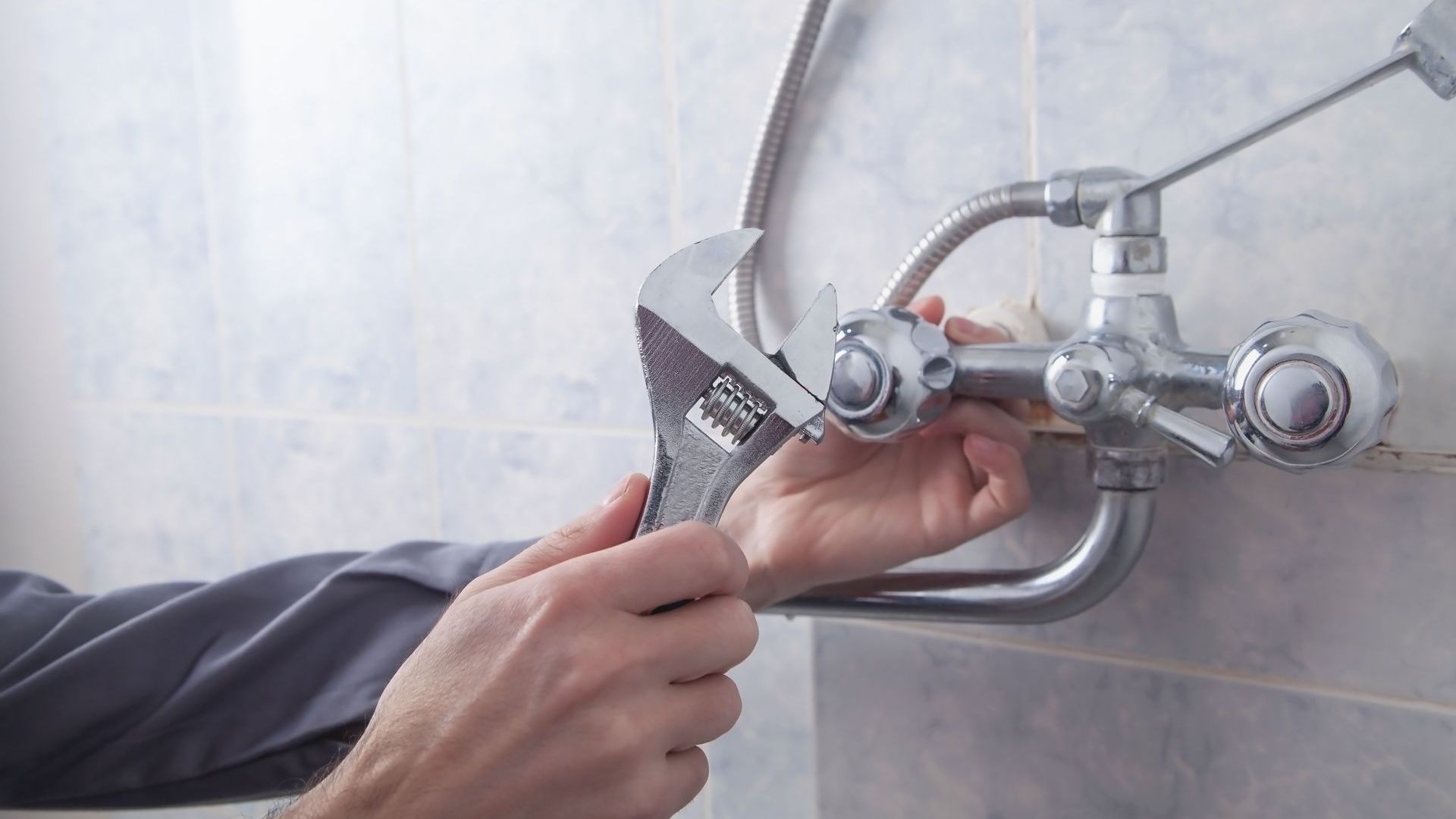 A man is fixing a faucet with a wrench in a bathroom.