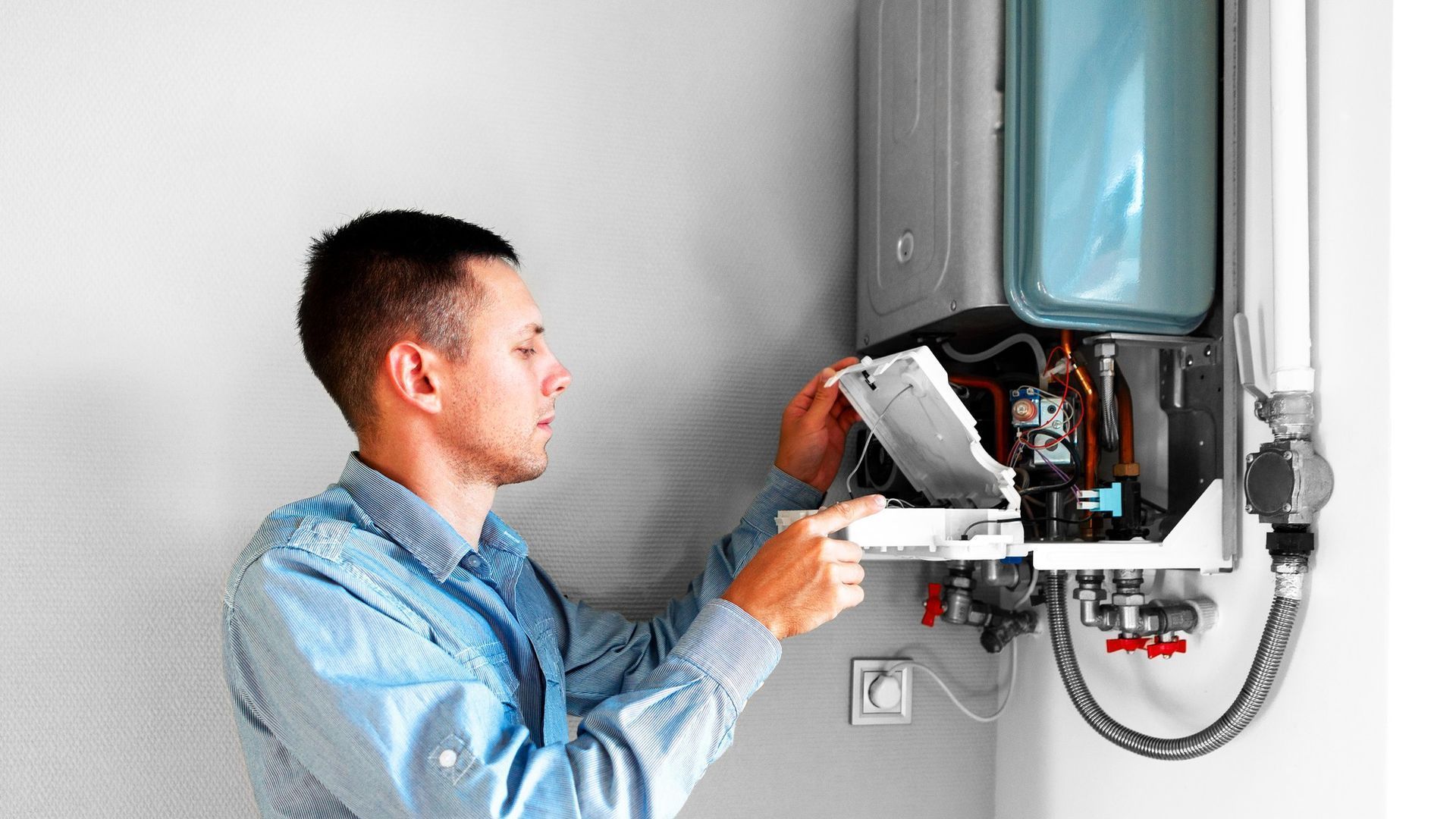 A man is fixing a water heater on a wall.
