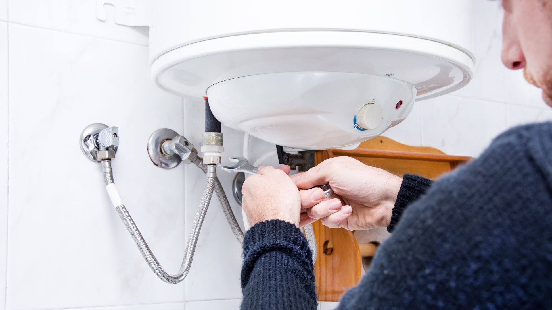 A man is fixing a water heater in a bathroom.