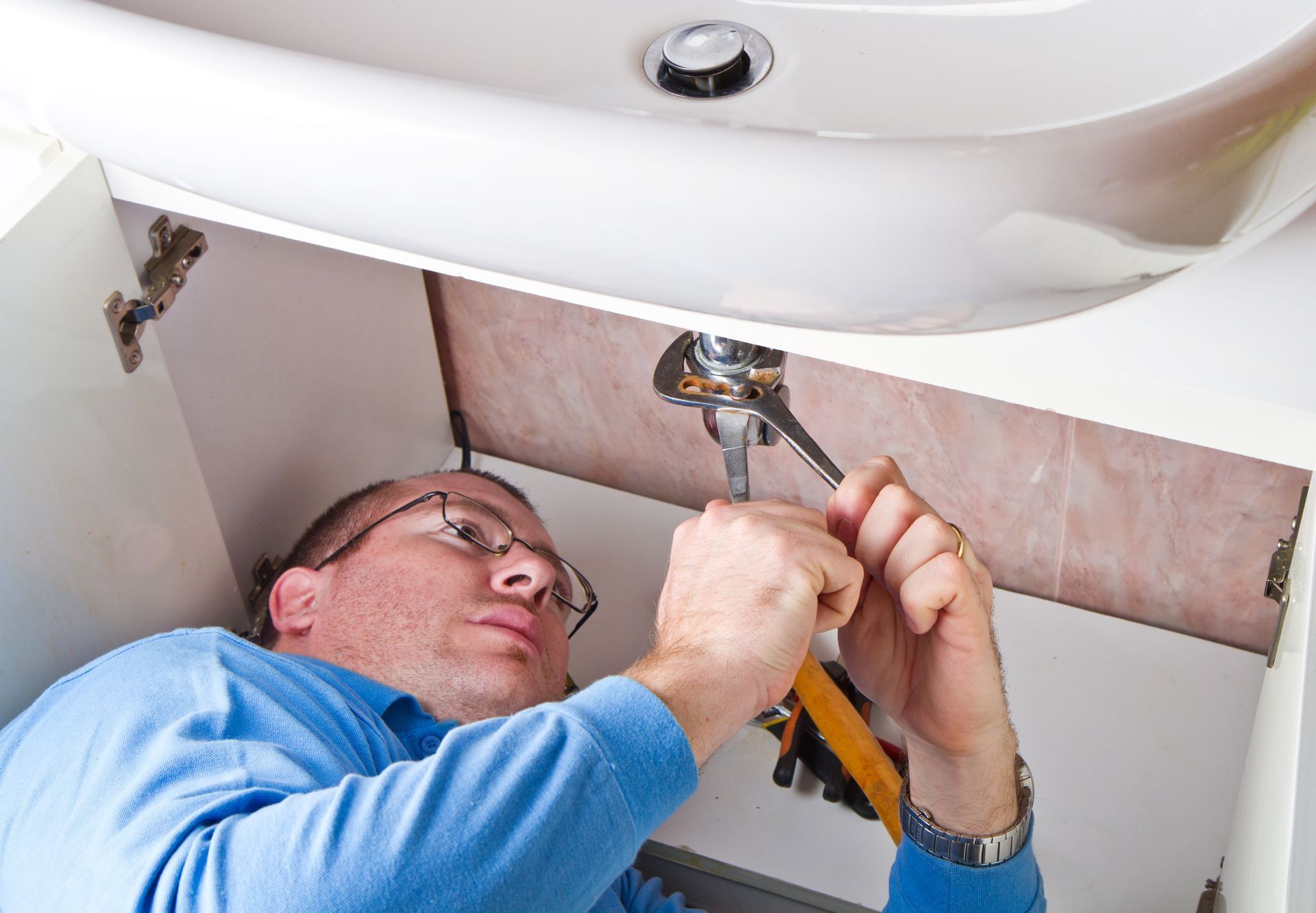 A man is fixing a sink with a wrench.