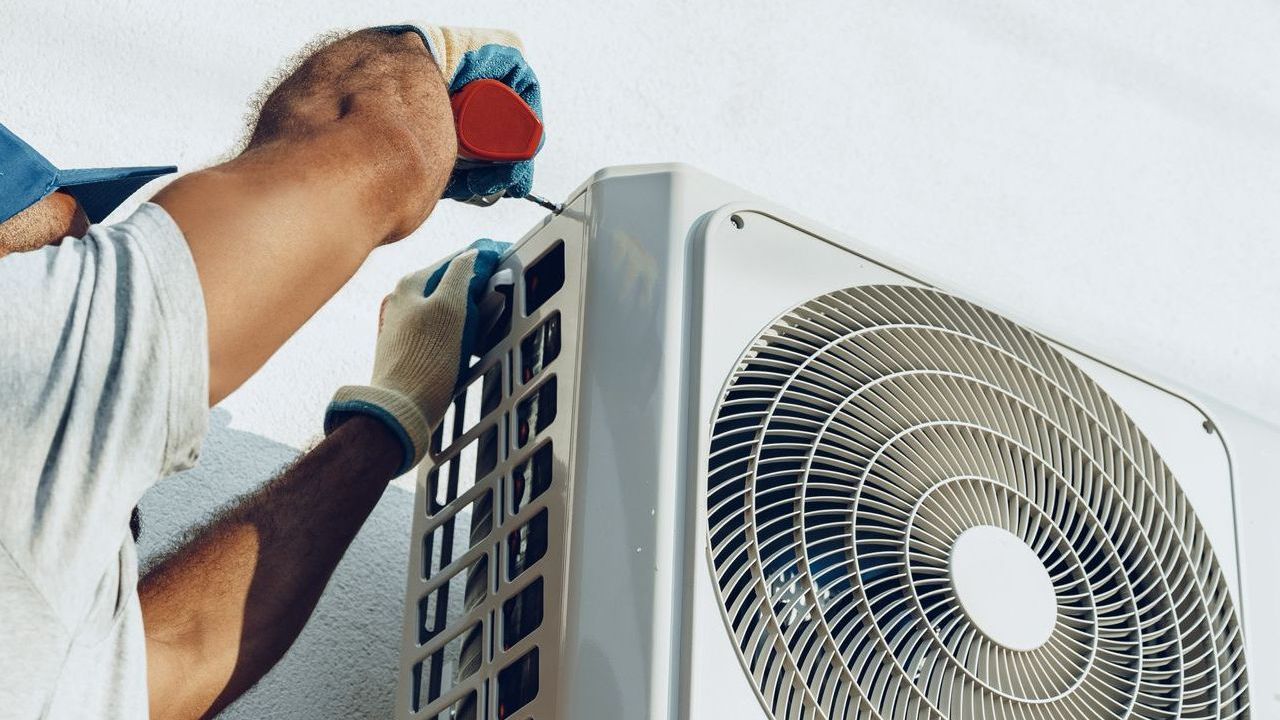 A man is fixing an air conditioner with a screwdriver.