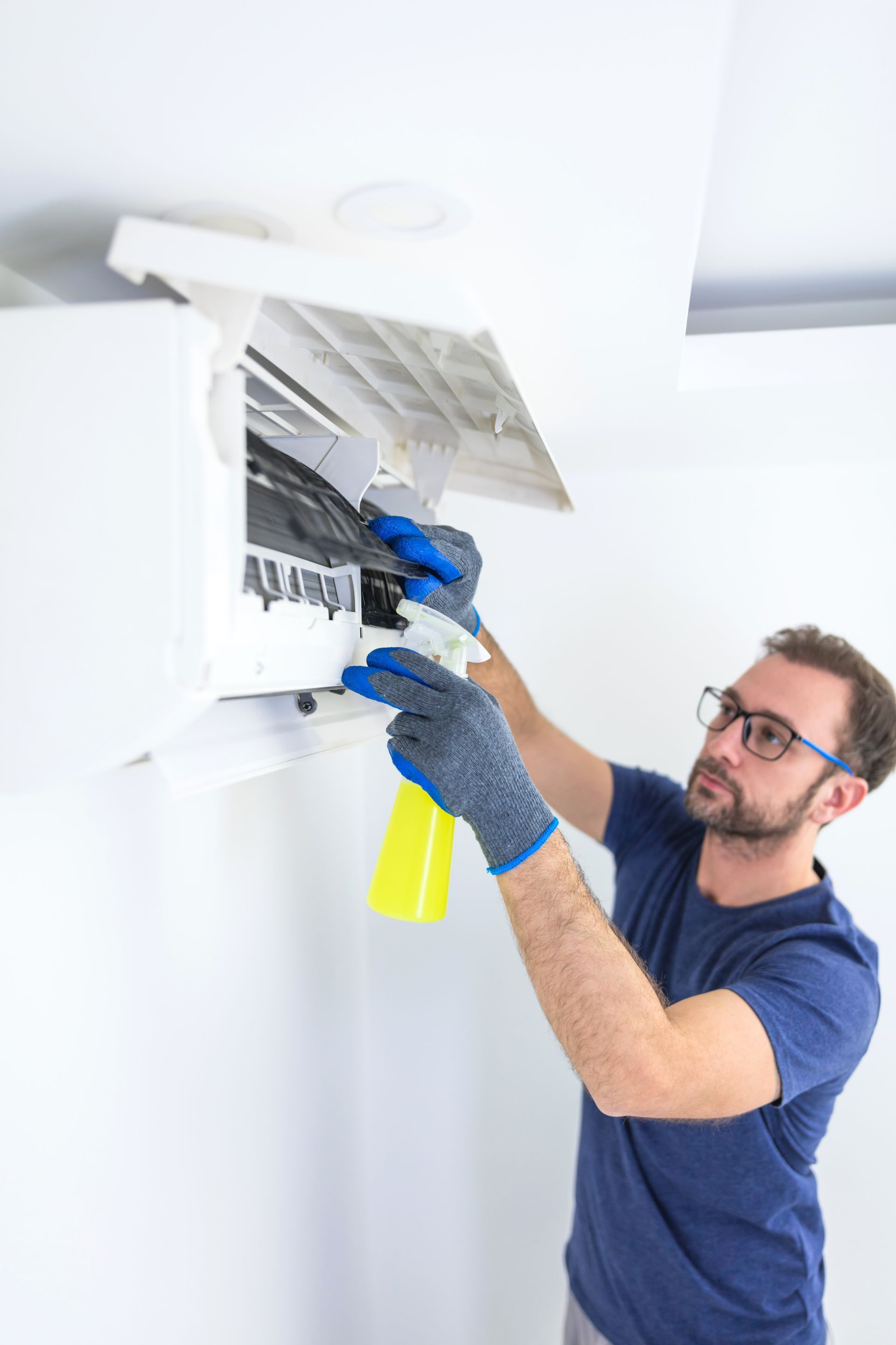 A man is cleaning an air conditioner with a spray bottle.