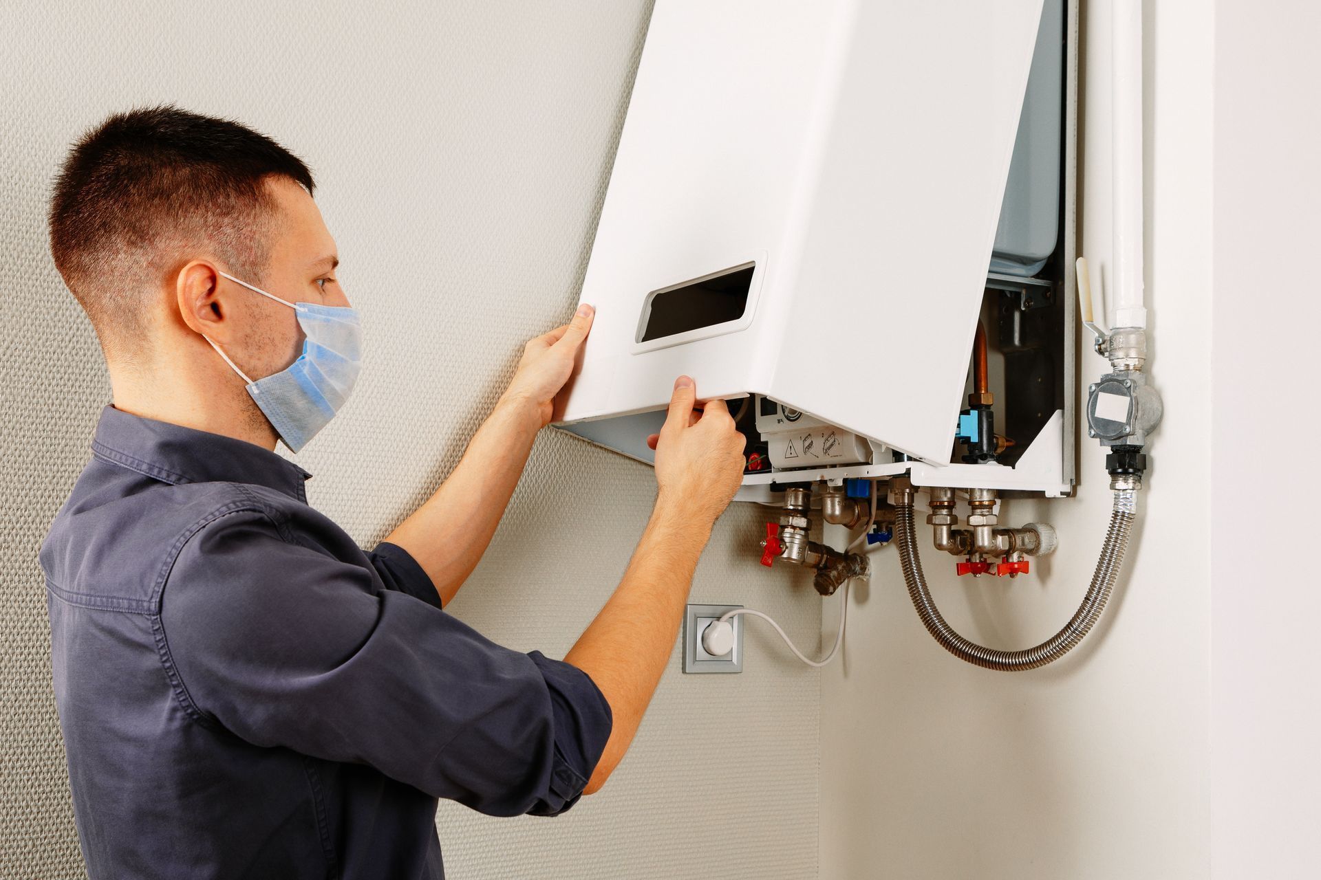 A man wearing a mask is fixing a water heater.