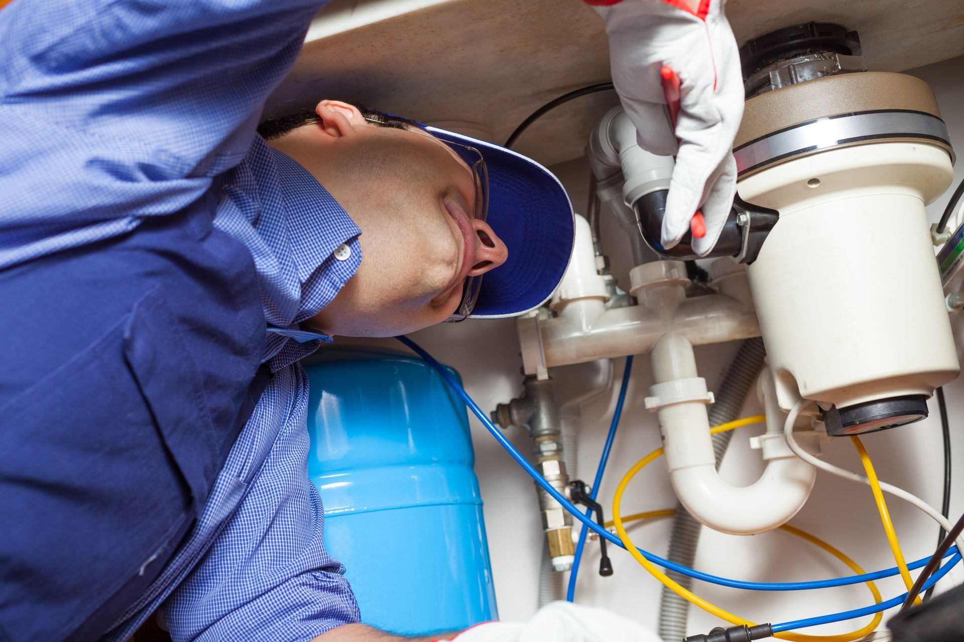 A man is working on a garbage disposal under a sink.