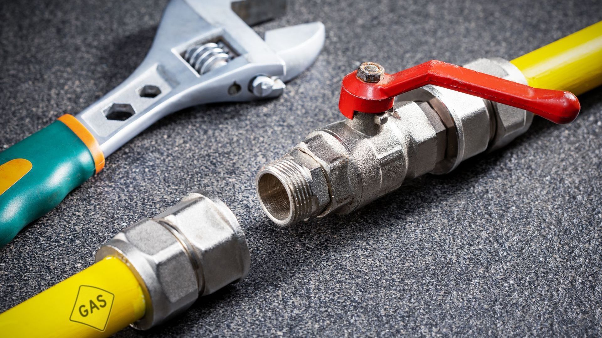 A close up of a gas pipe with a wrench and a valve.