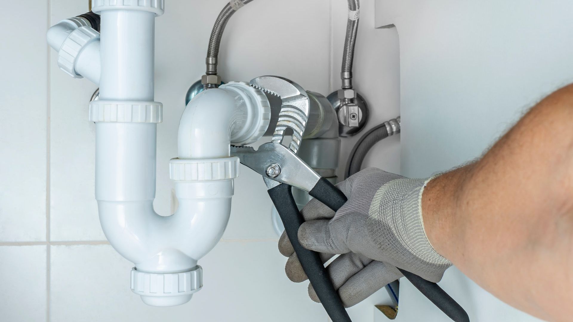 A plumber is fixing a sink pipe with a wrench.
