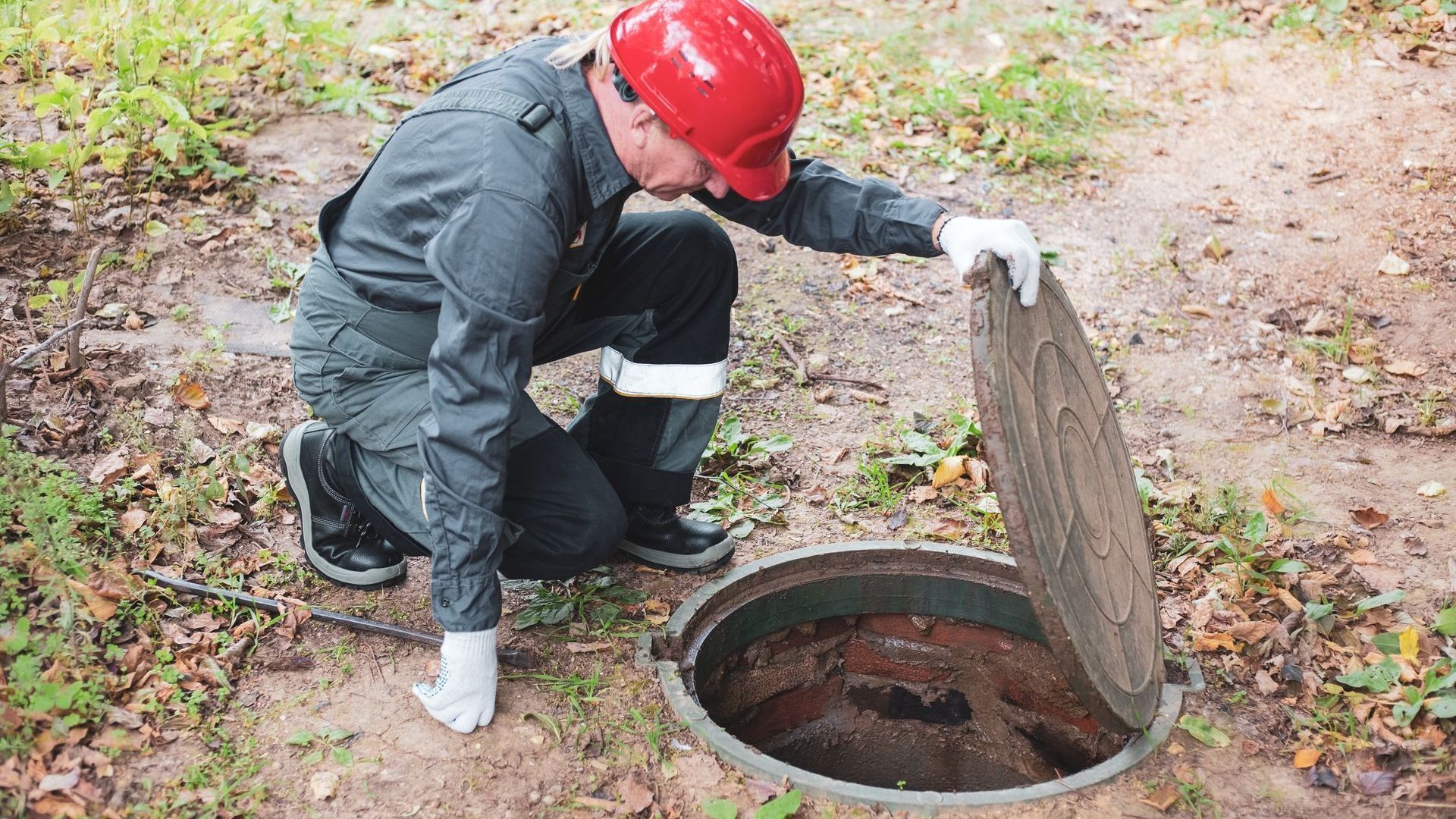 A man is kneeling down next to a manhole cover.
