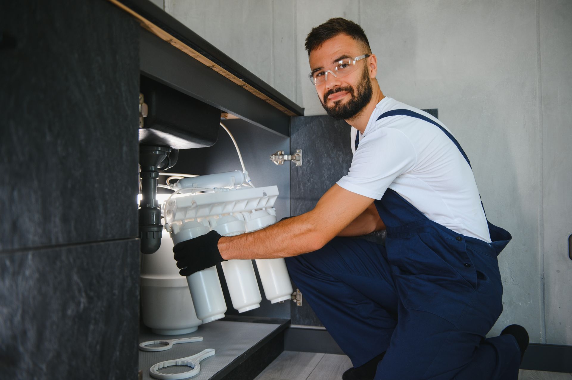 A man is installing a water filter under a sink in a kitchen.