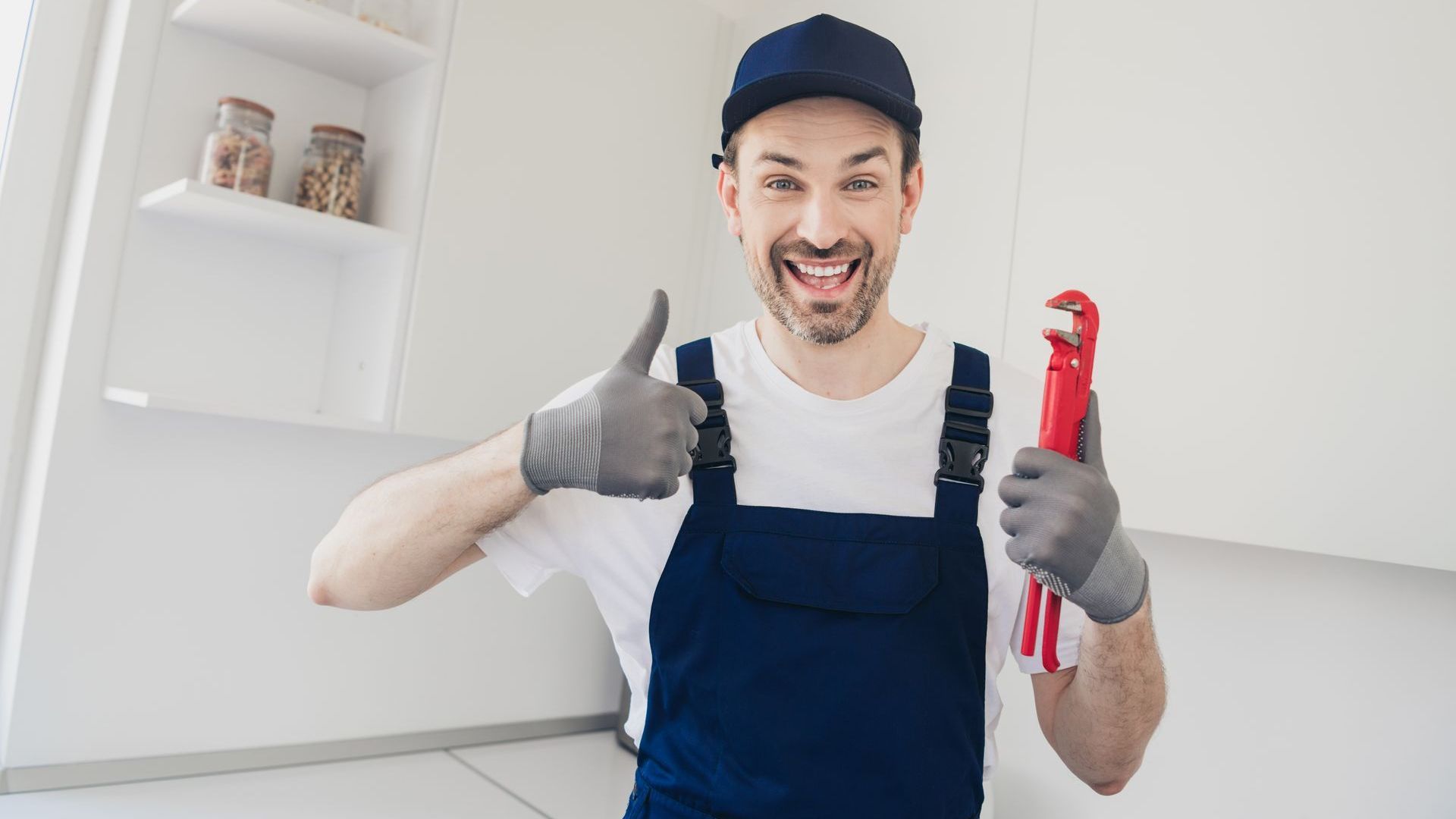 A plumber is holding a wrench and giving a thumbs up.