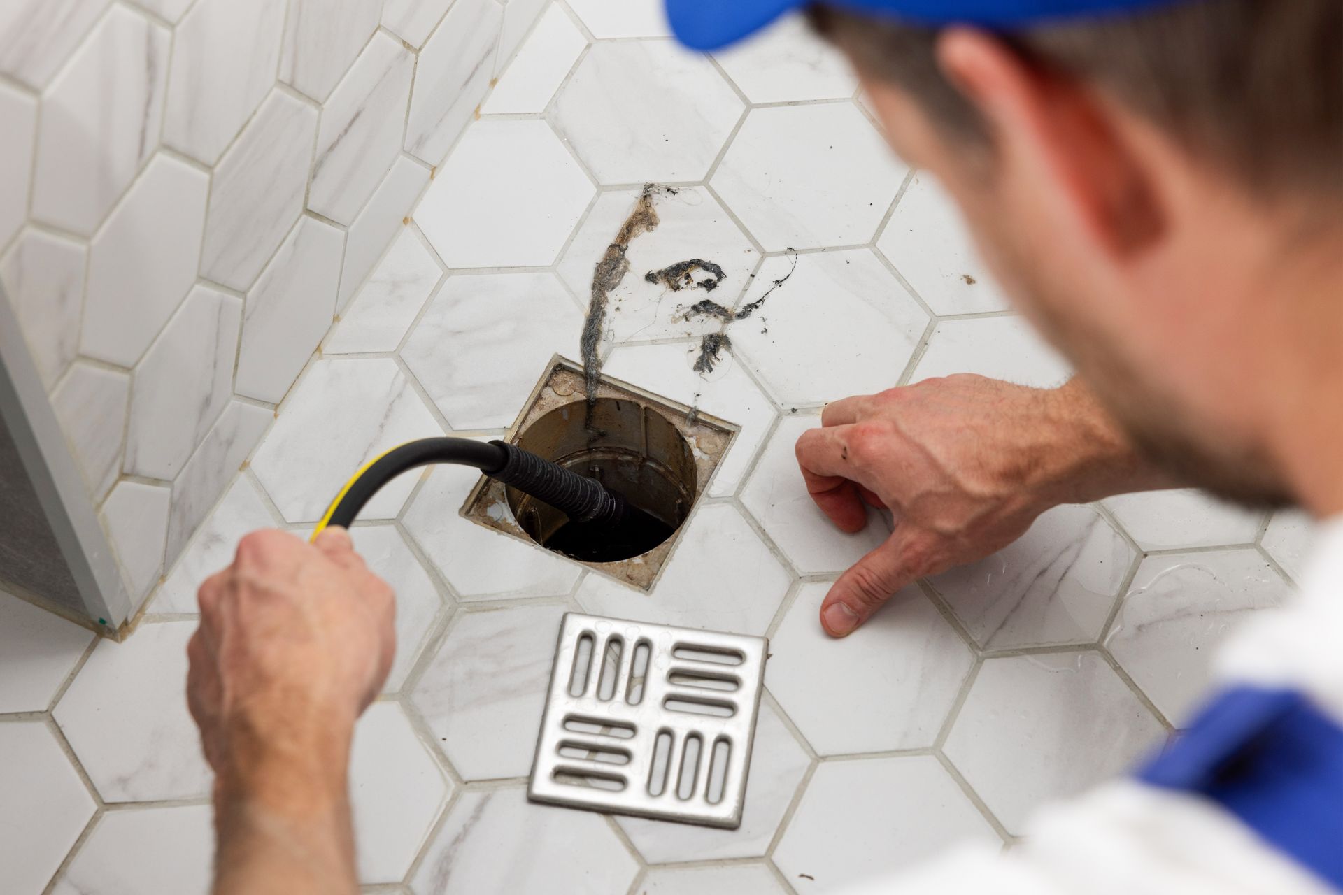 A man is fixing a drain in a bathroom with a hose.