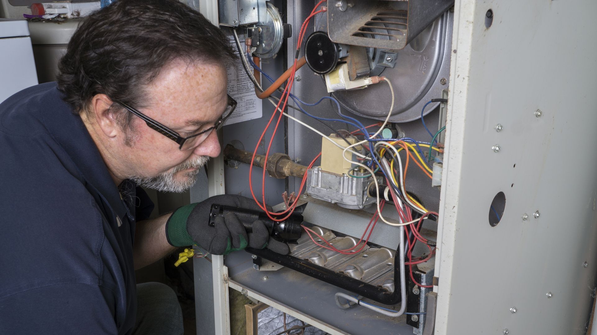 A man is working on an air conditioner with a screwdriver.