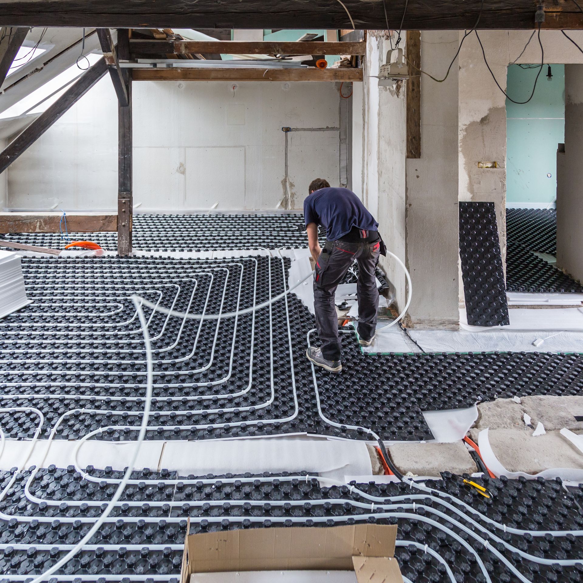 A man is working on a underfloor heating system in a room.