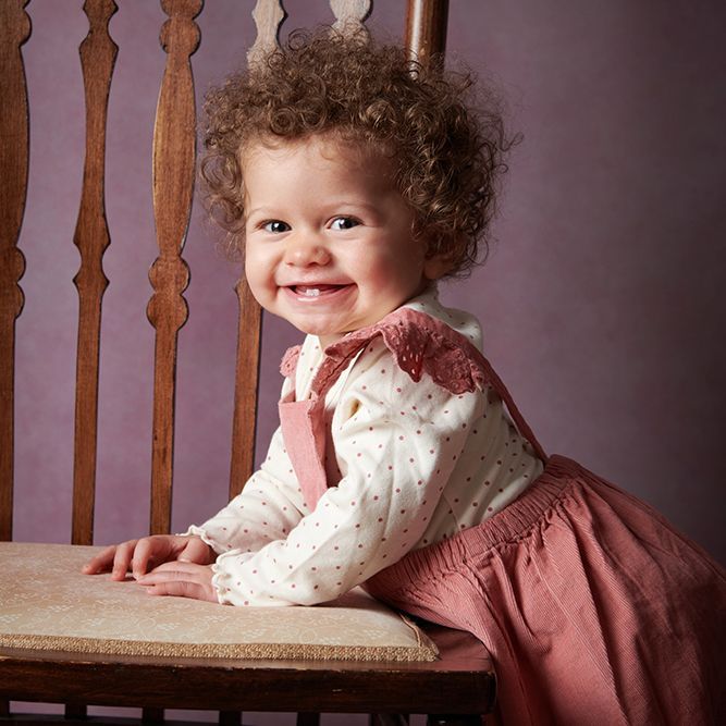 A little girl is sitting on a chair and smiling