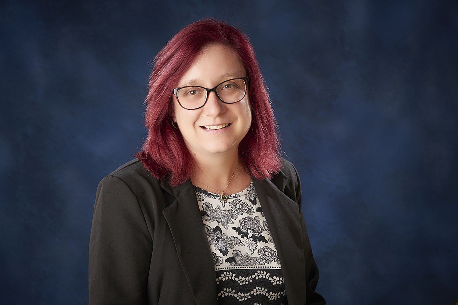 A woman with red hair and glasses is smiling for the camera.