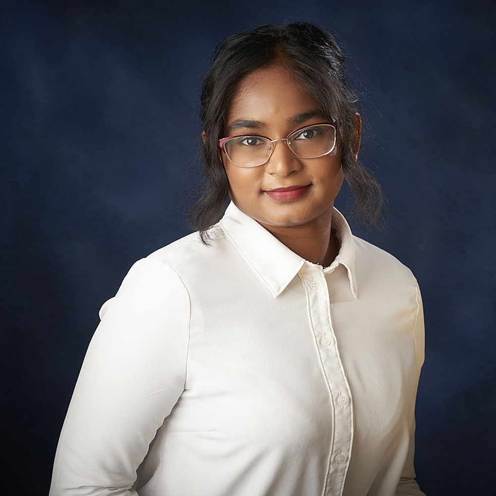 A woman wearing glasses and a white shirt is standing in front of a blue background.