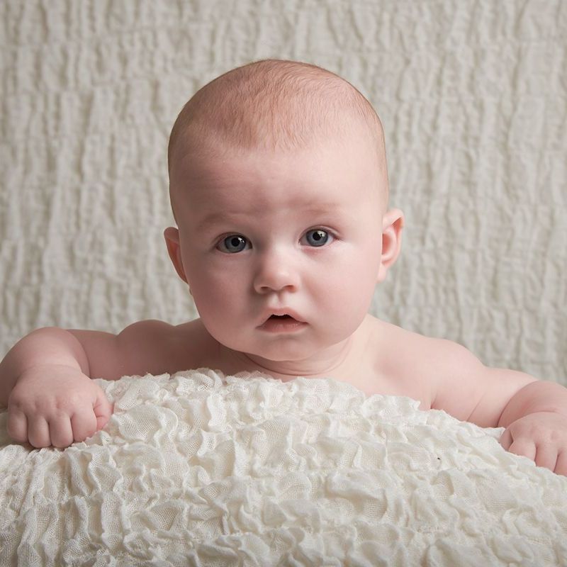 A baby is laying on a white blanket and smiling
