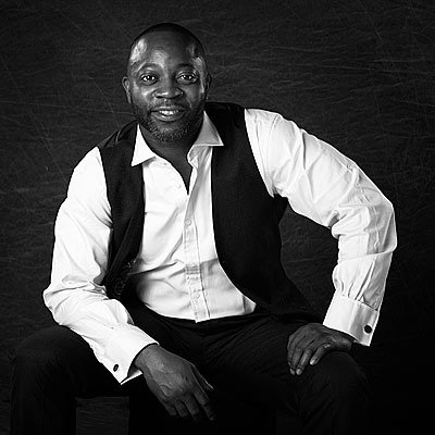 A man in a white shirt and black vest is sitting on a chair.