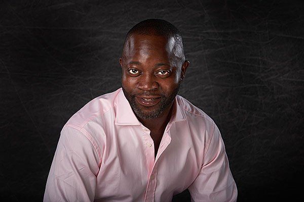 A man in a pink shirt is sitting in front of a blackboard.