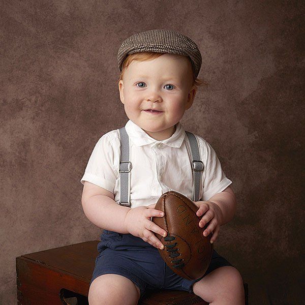 little boy smiling holding rugby ball and wearing flat cap Oakley Studios celebration photoshoot in Luton Bedfordshire