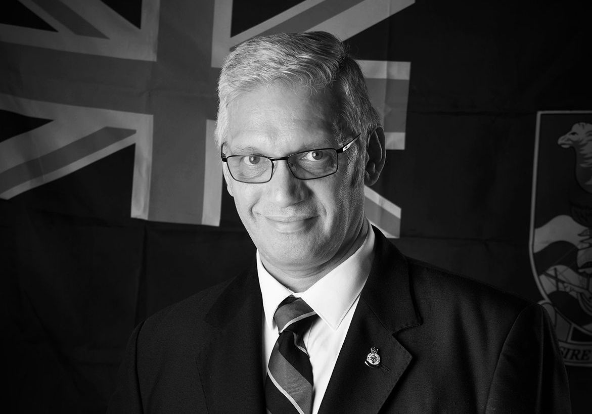 A man in a suit and tie is smiling in front of a british flag
