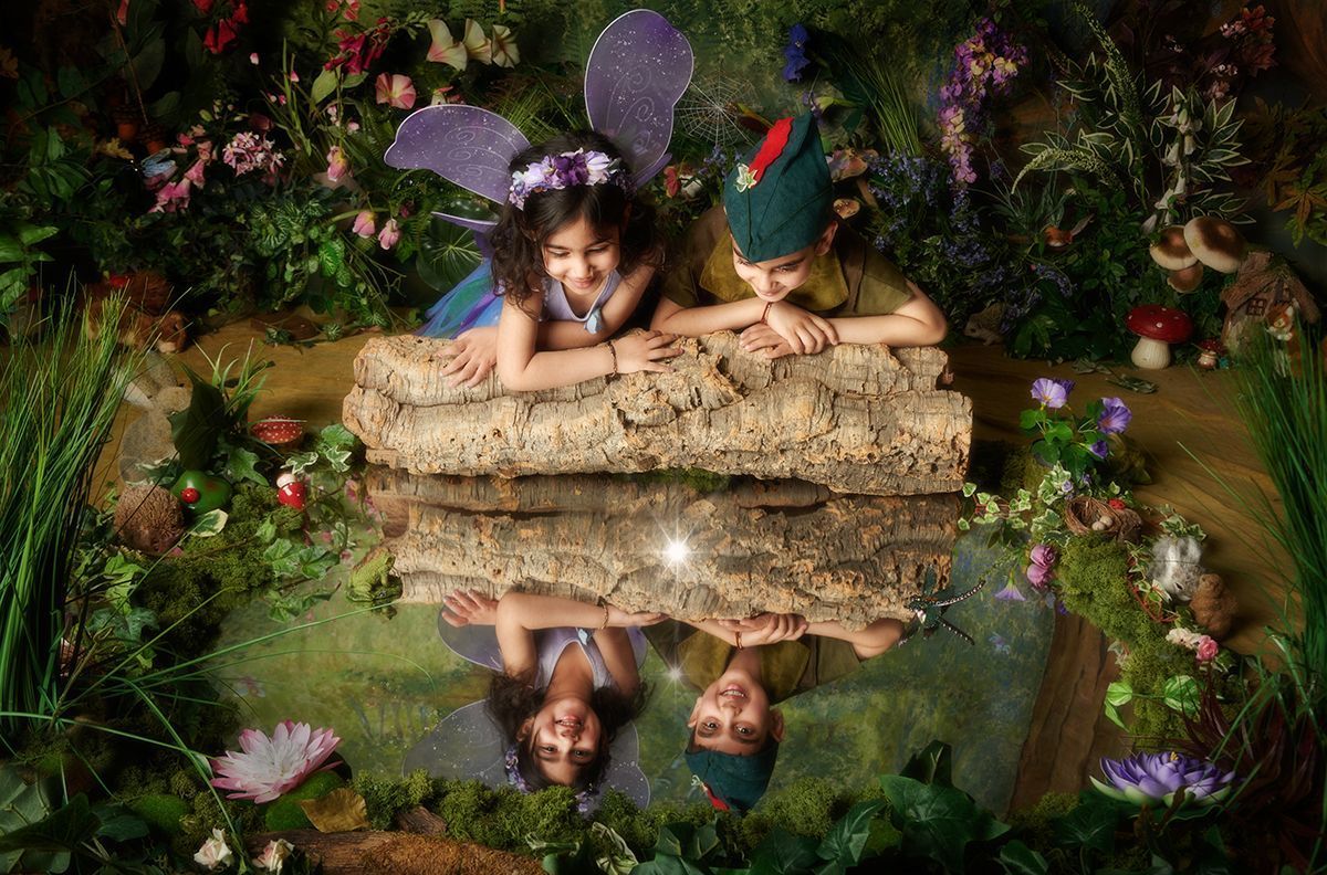 A boy and a girl in fairy costumes are laying on a log in a pond.