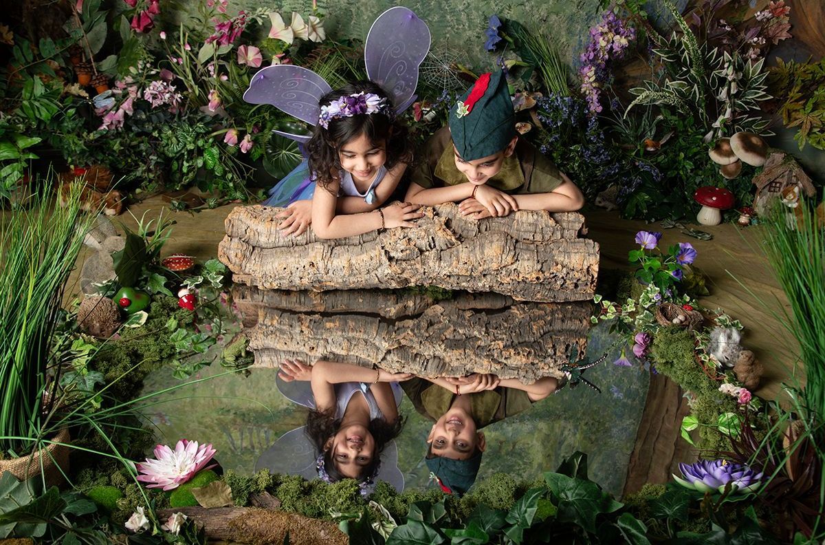 A group of children dressed as fairies are laying on a log.