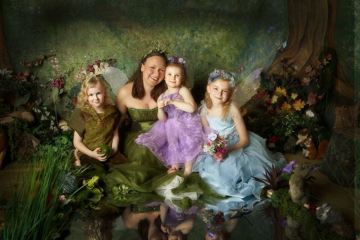 A woman and three little girls dressed as fairies are sitting next to each other in a forest.