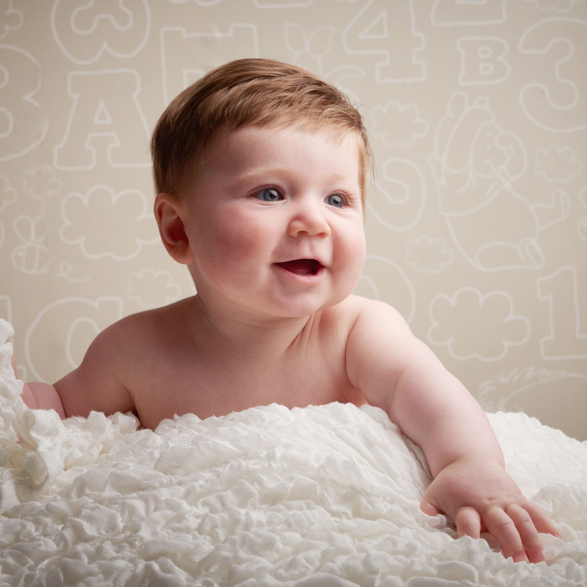 A baby is laying on a white blanket and smiling