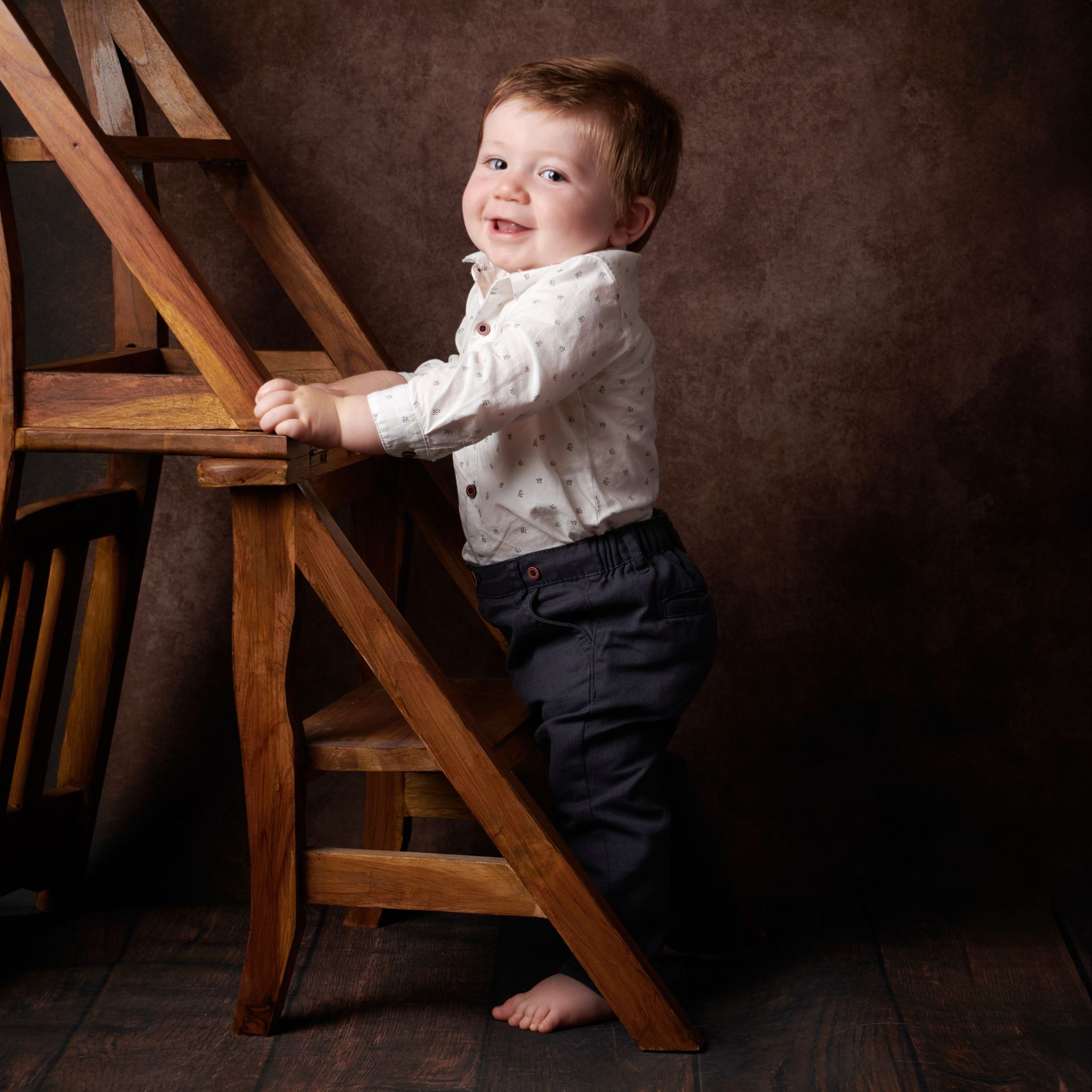 A little boy is standing on a wooden ladder