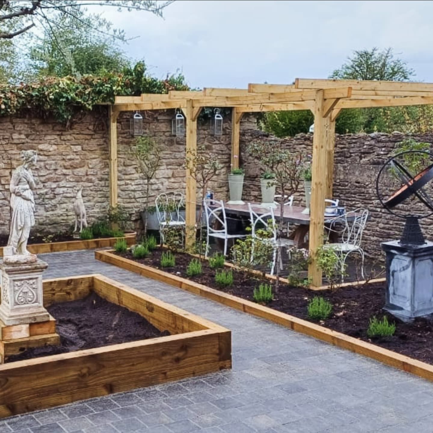 Outdoor dining area with a wooden pergola, stone wall, and a statue.