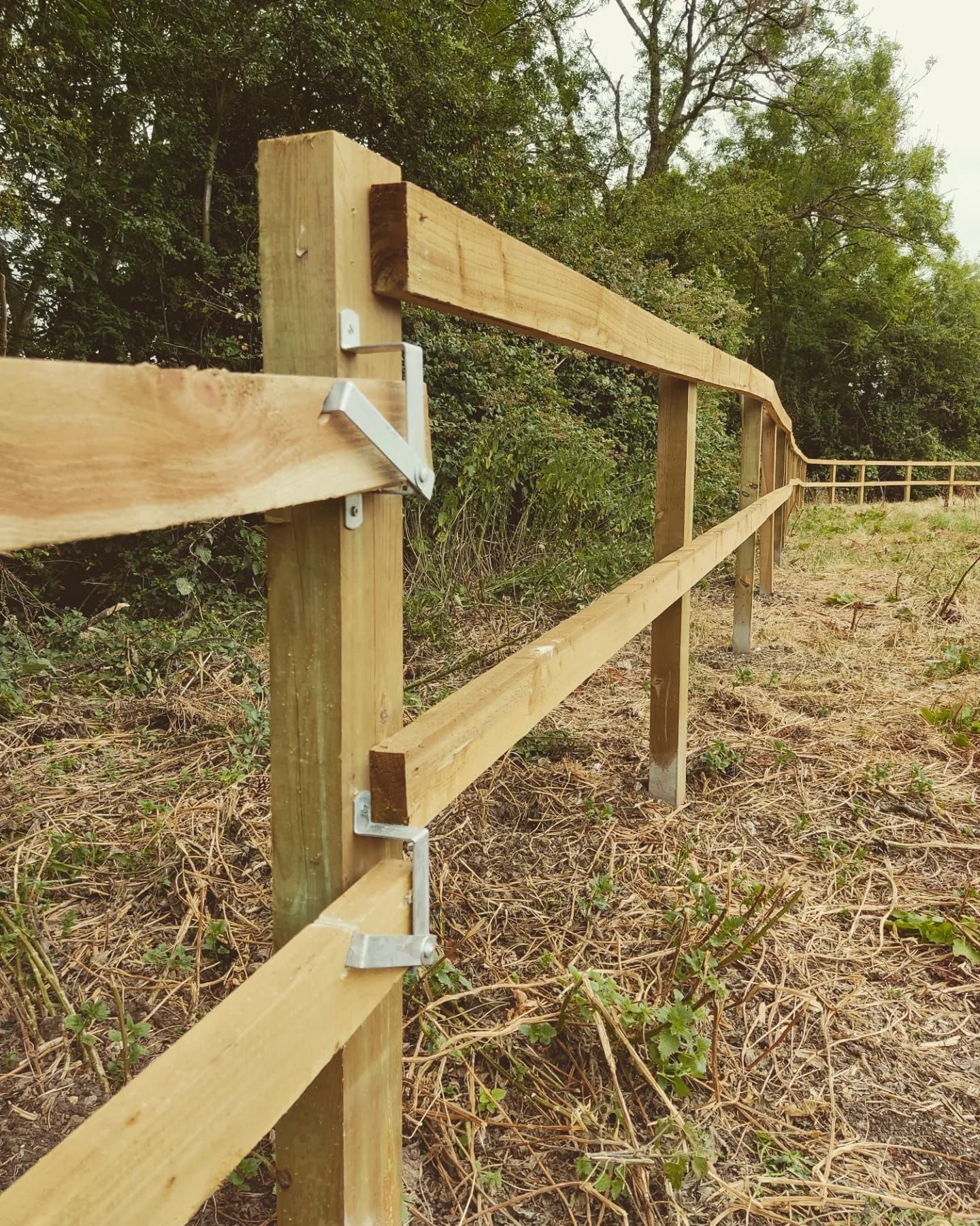 Wooden fence with two horizontal rails, secured by metal brackets, outdoors.