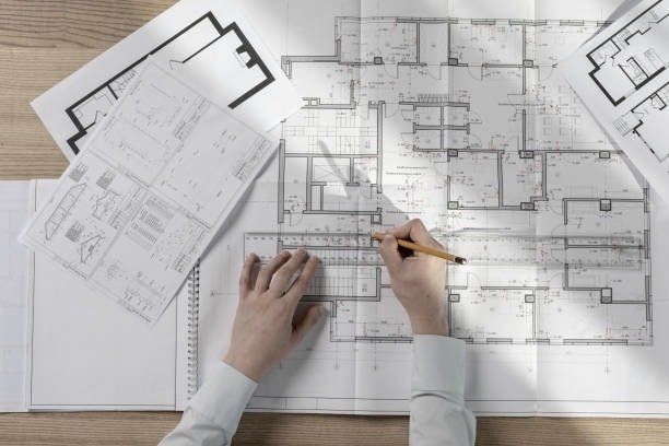 Hands sketching architectural plans on a wooden desk, using a ruler and pencil.